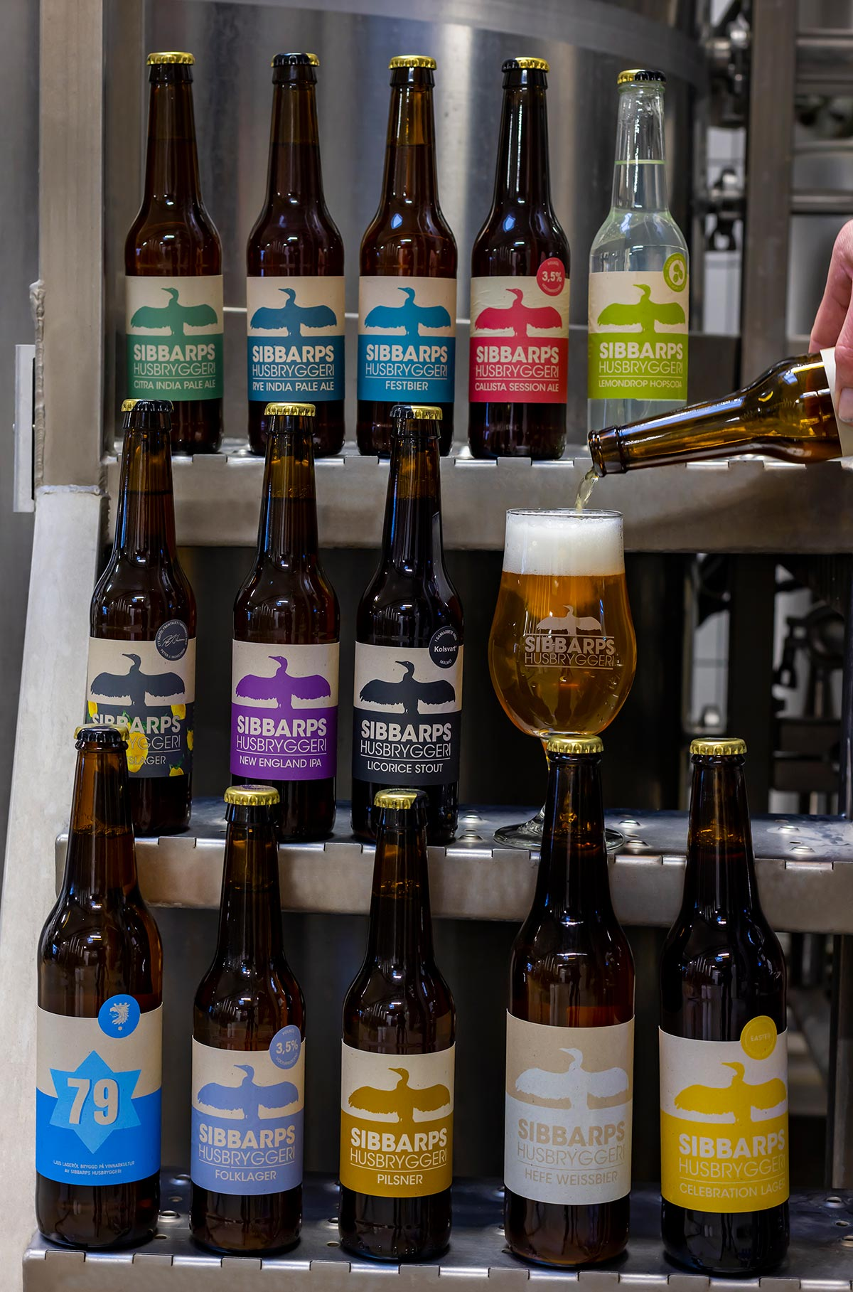 Sibbarps Husbryggeris sortiment av flaskor uppställda på bryggeriets stålhyllor — IPA, lager, stout och säsongsöl