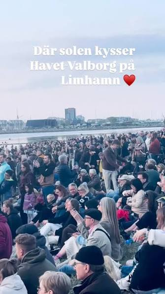 Publik sitter i gräset på Limhamns strandäng med Malmös siluett i bakgrunden — Valborg vid havet